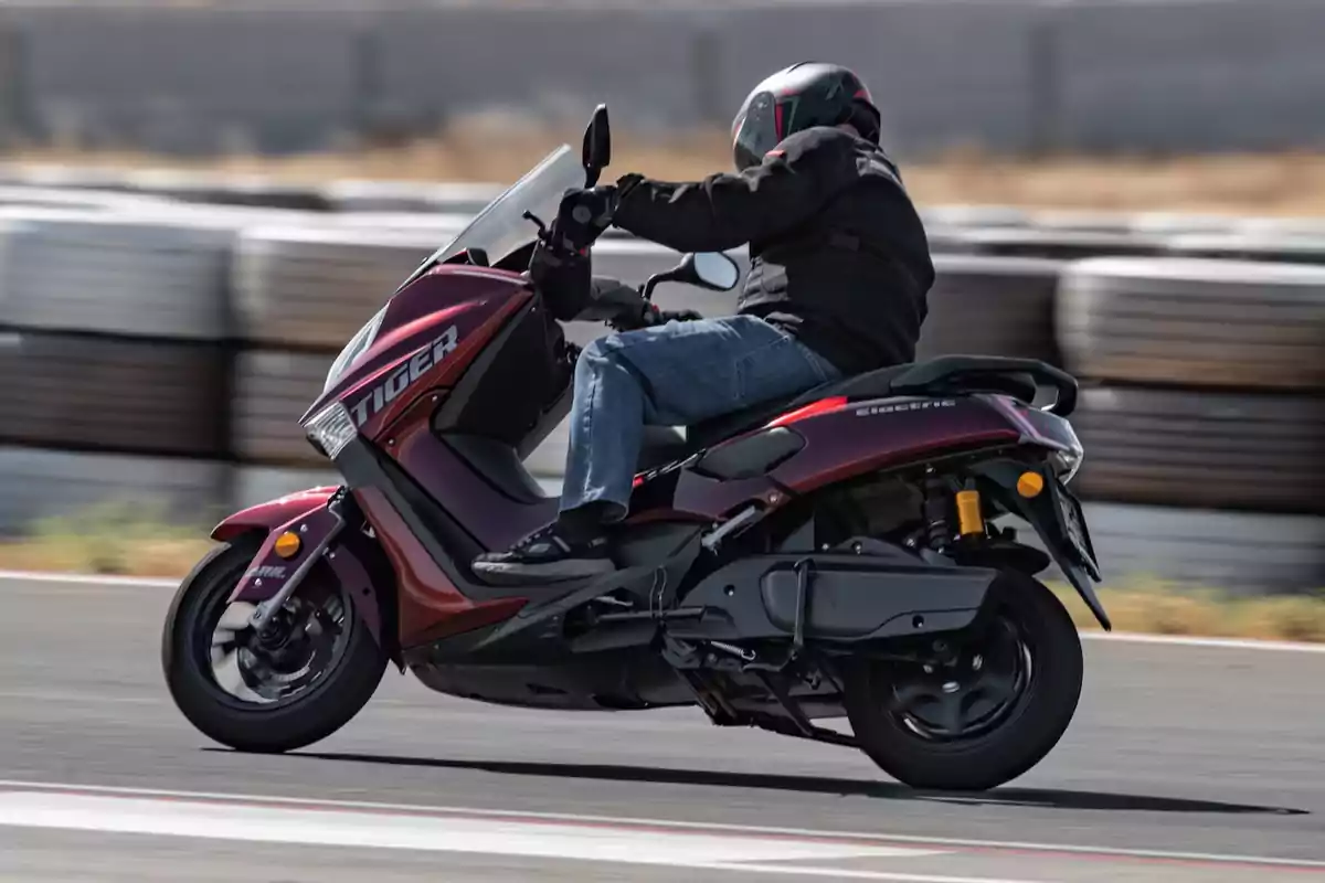 Persona conduciendo una motocicleta eléctrica color vino en una pista de asfalto con fondo de llantas apiladas Persona conduciendo una motocicleta eléctrica color vino en una pista de asfalto con fondo de llantas apiladas