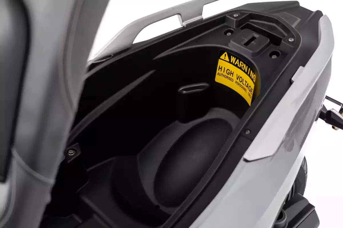 Compartimento de almacenamiento debajo del asiento de una motocicleta eléctrica con una advertencia de alto voltaje. Compartimento de almacenamiento debajo del asiento de una motocicleta eléctrica con una advertencia de alto voltaje.