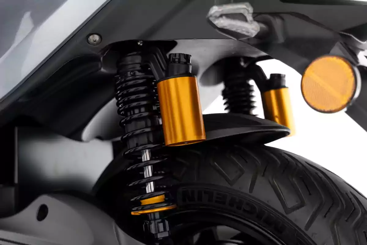 Detalle de la suspensión trasera de una motocicleta con amortiguadores de resorte y componentes en color dorado junto a una llanta Michelin Detalle de la suspensión trasera de una motocicleta con amortiguadores de resorte y componentes en color dorado junto a una llanta Michelin