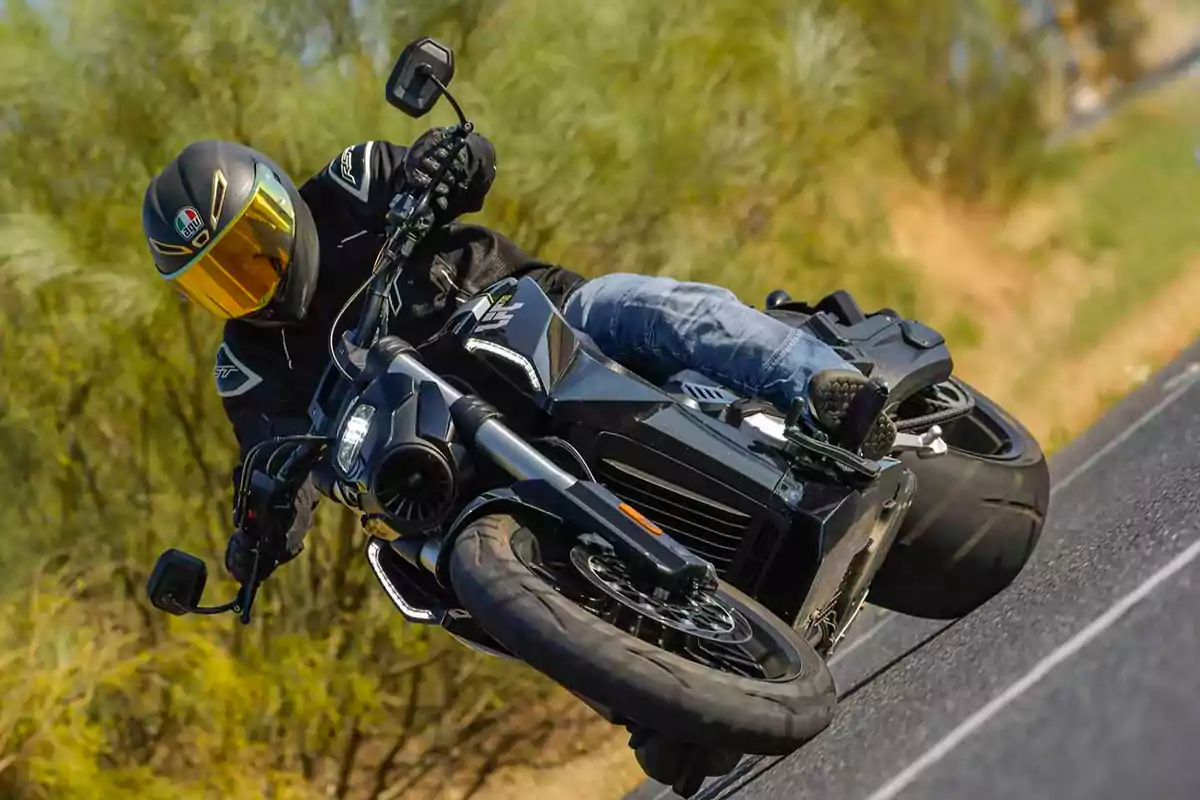 Persona con casco y ropa de protección conduciendo una motocicleta negra en una curva sobre una carretera asfaltada