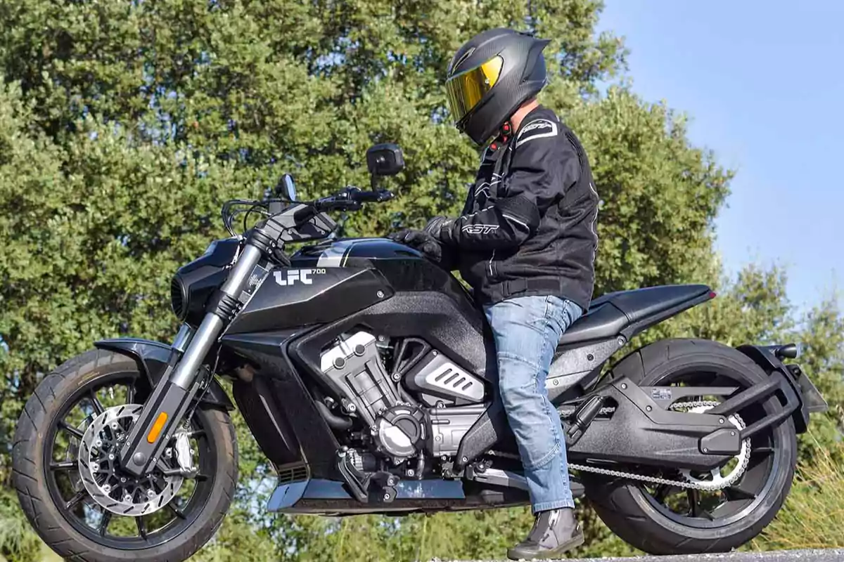 Persona con casco y chaqueta negra sentada sobre una motocicleta negra LFC700 en un entorno al aire libre con árboles de fondo Persona con casco y chaqueta negra sentada sobre una motocicleta negra LFC700 en un entorno al aire libre con árboles de fondo
