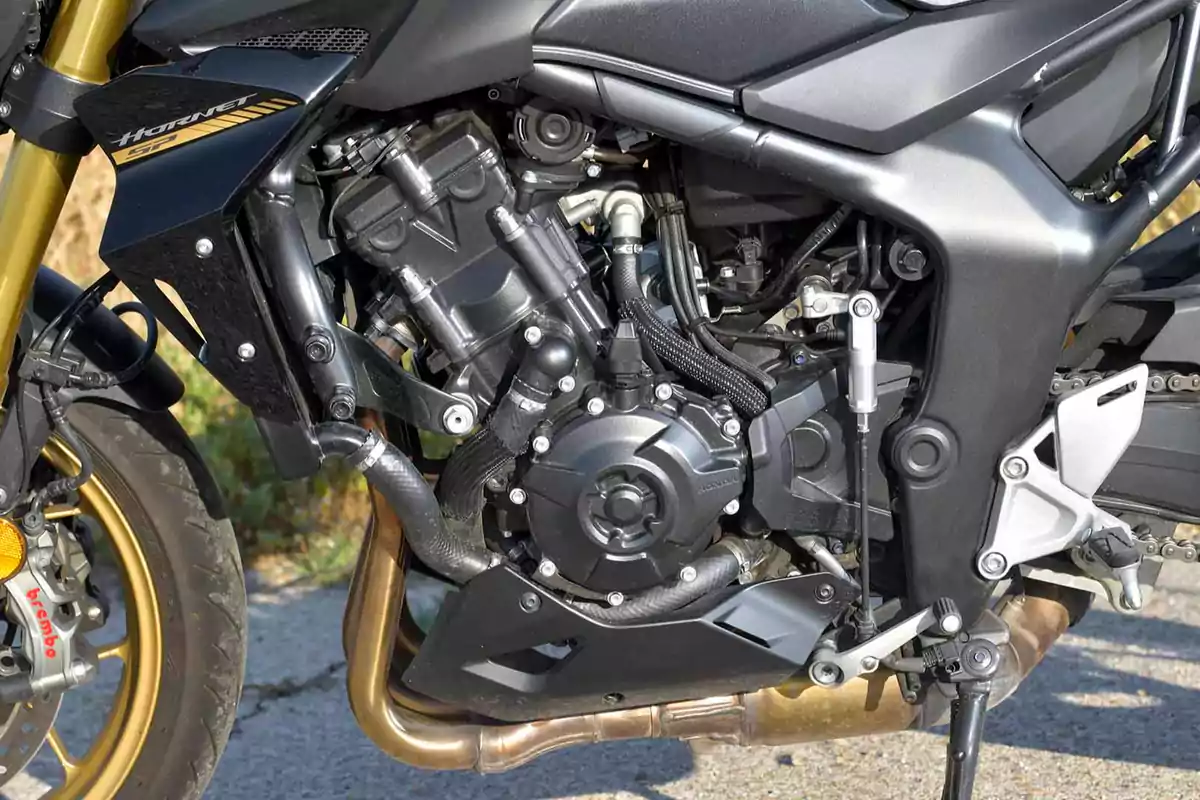 Detalle del motor de una motocicleta Honda Hornet con componentes visibles y parte del chasis en color negro y dorado Detalle del motor de una motocicleta Honda Hornet con componentes visibles y parte del chasis en color negro y dorado