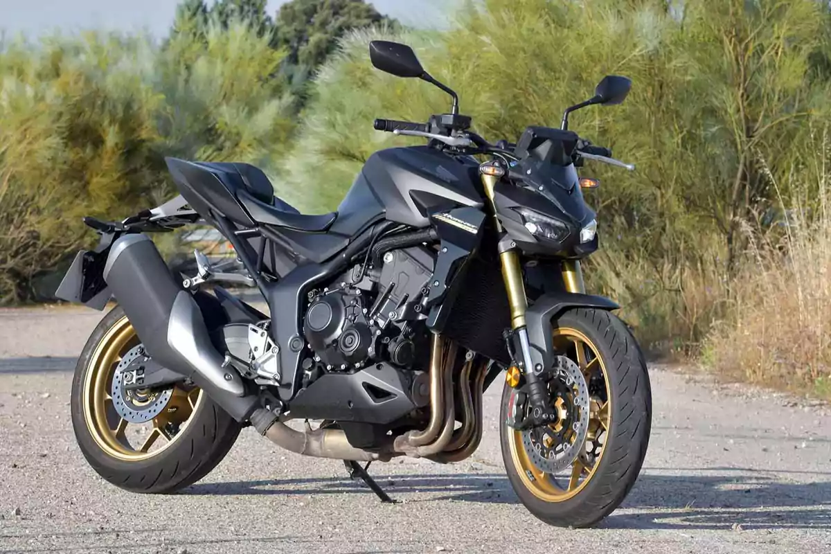 Motocicleta deportiva negra con detalles dorados estacionada en un camino al aire libre rodeado de vegetación Motocicleta deportiva negra con detalles dorados estacionada en un camino al aire libre rodeado de vegetación