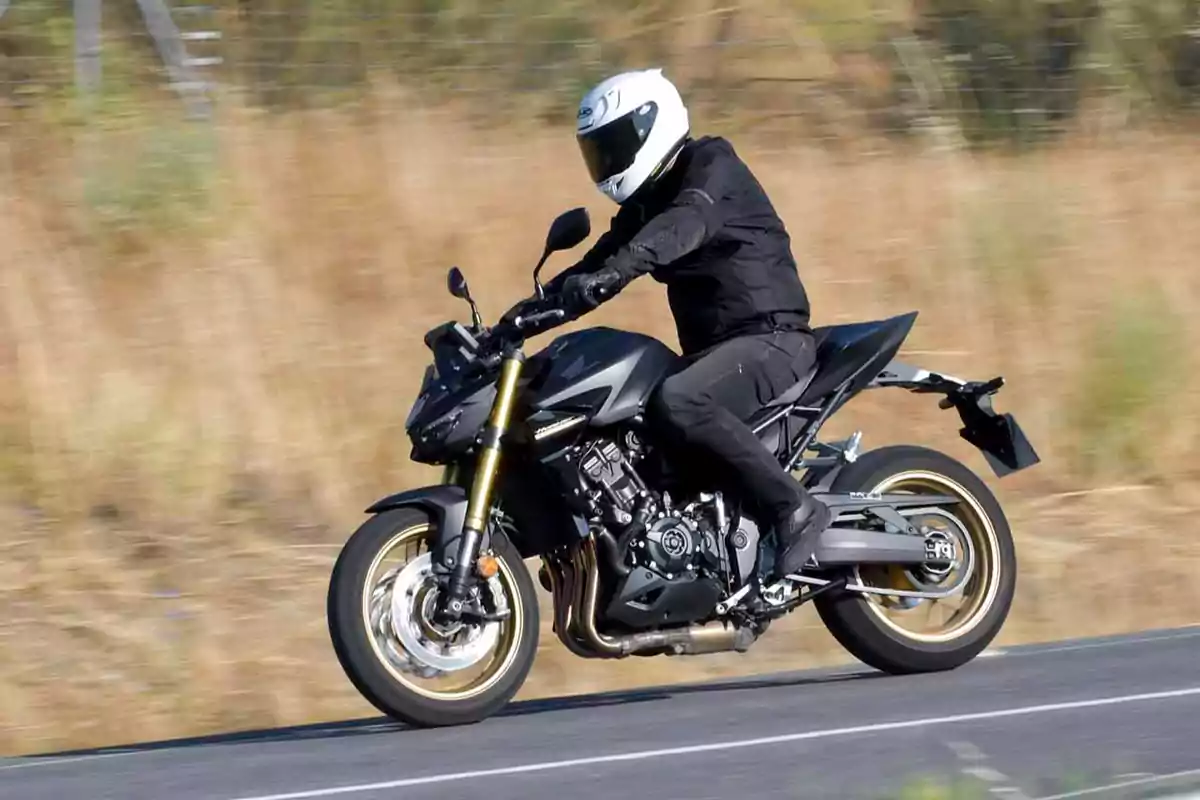 Persona conduciendo una motocicleta negra en una carretera con fondo de vegetación seca Persona conduciendo una motocicleta negra en una carretera con fondo de vegetación seca
