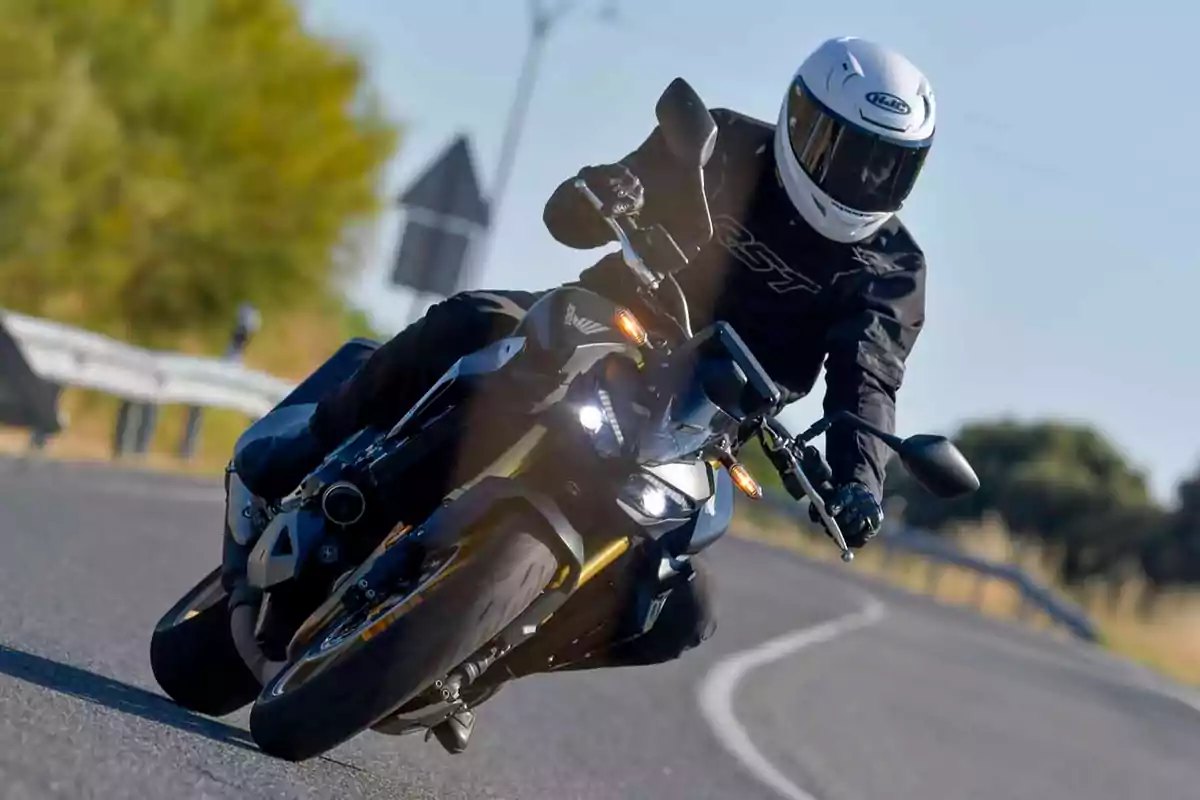 Persona con casco blanco y ropa de protección negra conduciendo una motocicleta deportiva en una carretera curva durante el día Persona con casco blanco y ropa de protección negra conduciendo una motocicleta deportiva en una carretera curva durante el día