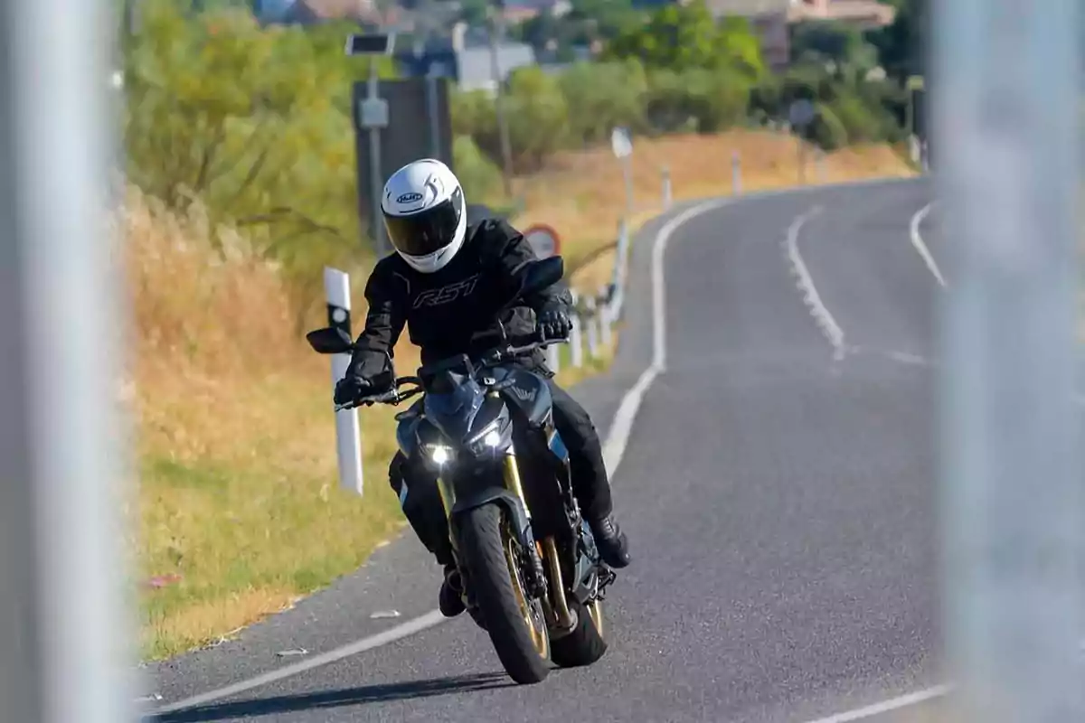 Persona con casco y ropa de protección conduciendo una motocicleta en una carretera curva rodeada de vegetación Persona con casco y ropa de protección conduciendo una motocicleta en una carretera curva rodeada de vegetación