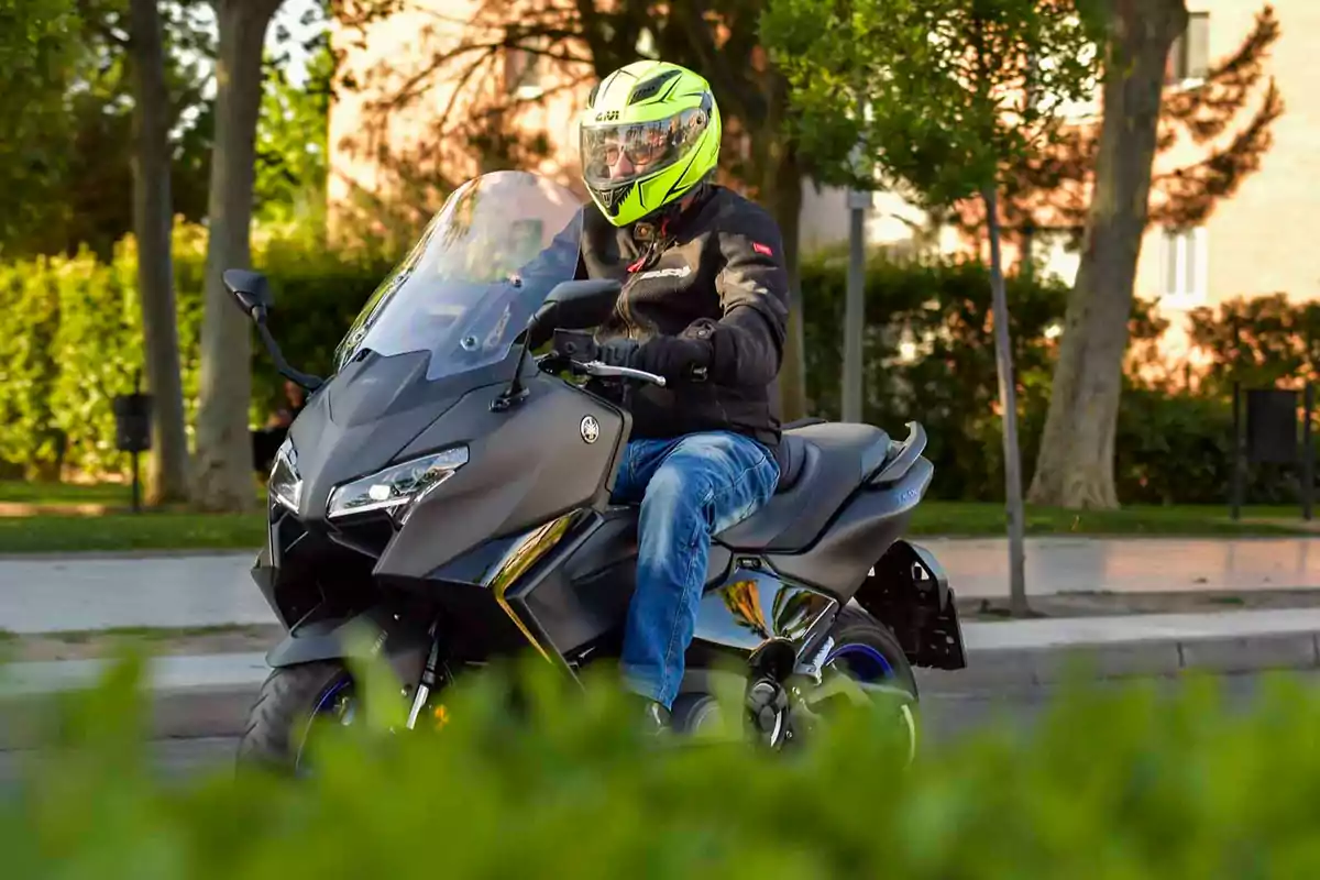 Persona conduciendo una motocicleta negra con casco amarillo en una calle rodeada de árboles y vegetación Persona conduciendo una motocicleta negra con casco amarillo en una calle rodeada de árboles y vegetación