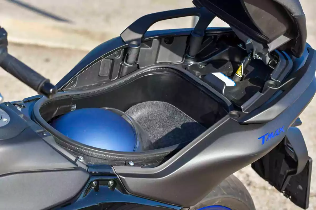 Compartimento de almacenamiento bajo el asiento de una motocicleta con un casco azul guardado en su interior Compartimento de almacenamiento bajo el asiento de una motocicleta con un casco azul guardado en su interior
