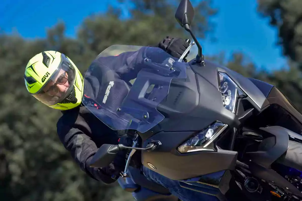 Persona con casco amarillo y chaqueta negra conduciendo una motocicleta Yamaha negra en un día soleado