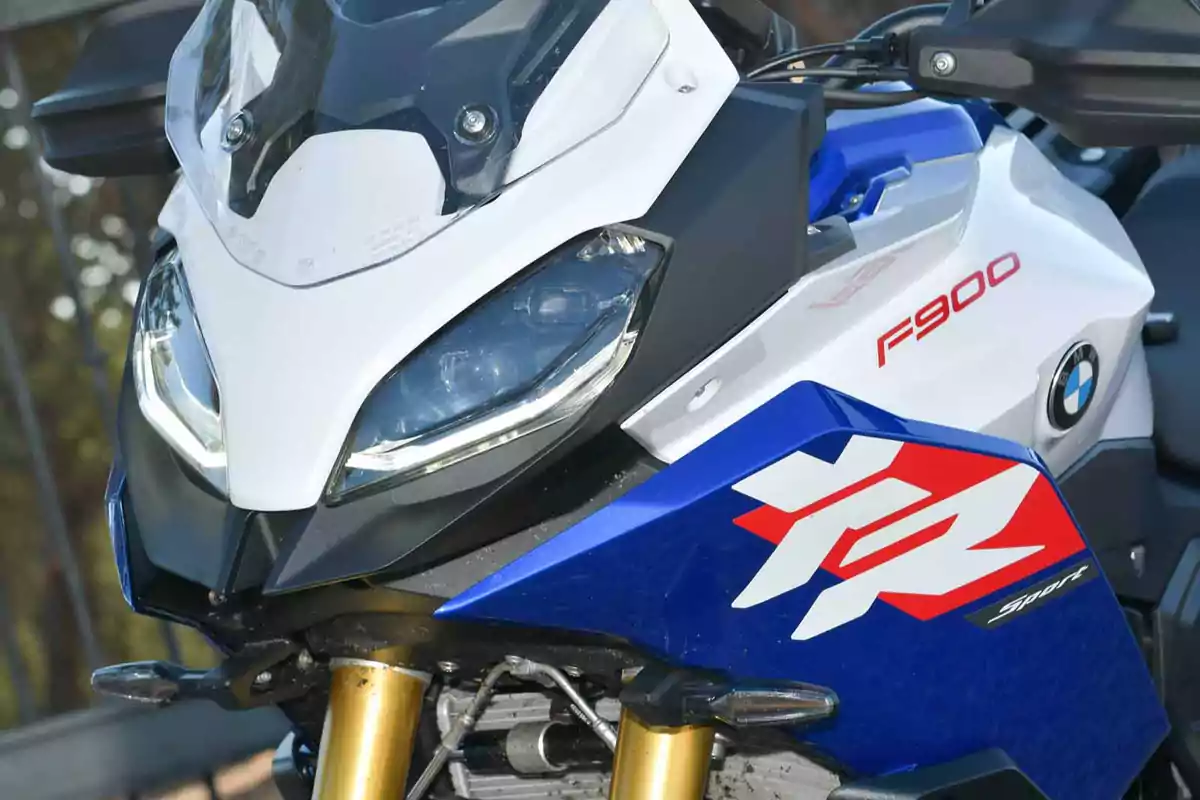 Motocicleta deportiva BMW F900 XR en colores blanco, azul y rojo vista de cerca mostrando el carenado y el faro delantero Motocicleta deportiva BMW F900 XR en colores blanco, azul y rojo vista de cerca mostrando el carenado y el faro delantero
