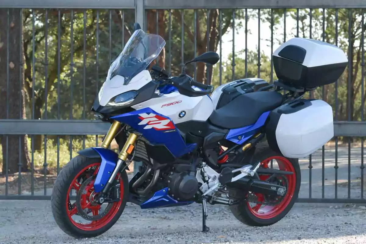 Motocicleta deportiva BMW azul con maletas laterales y trasera estacionada frente a una reja de metal Motocicleta deportiva BMW azul con maletas laterales y trasera estacionada frente a una reja de metal