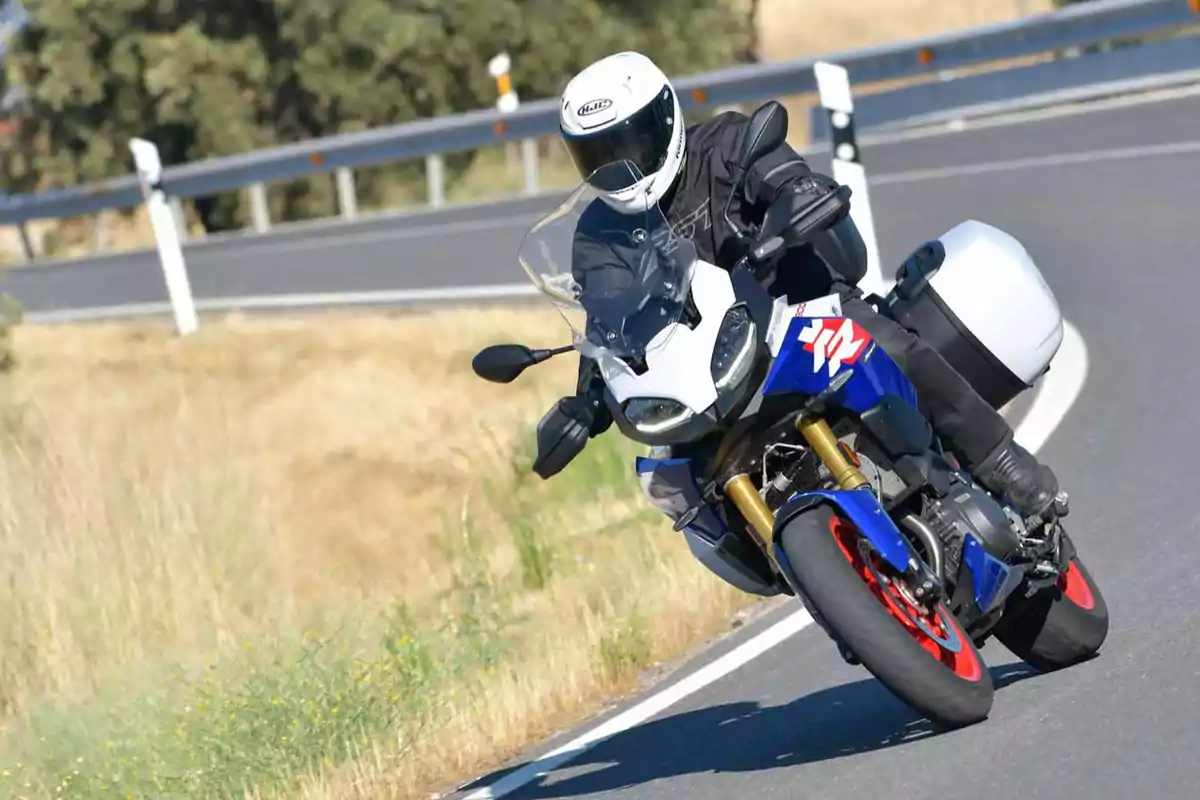 Persona conduciendo una motocicleta deportiva azul con maletas laterales en una carretera curva rodeada de vegetación seca Persona conduciendo una motocicleta deportiva azul con maletas laterales en una carretera curva rodeada de vegetación seca