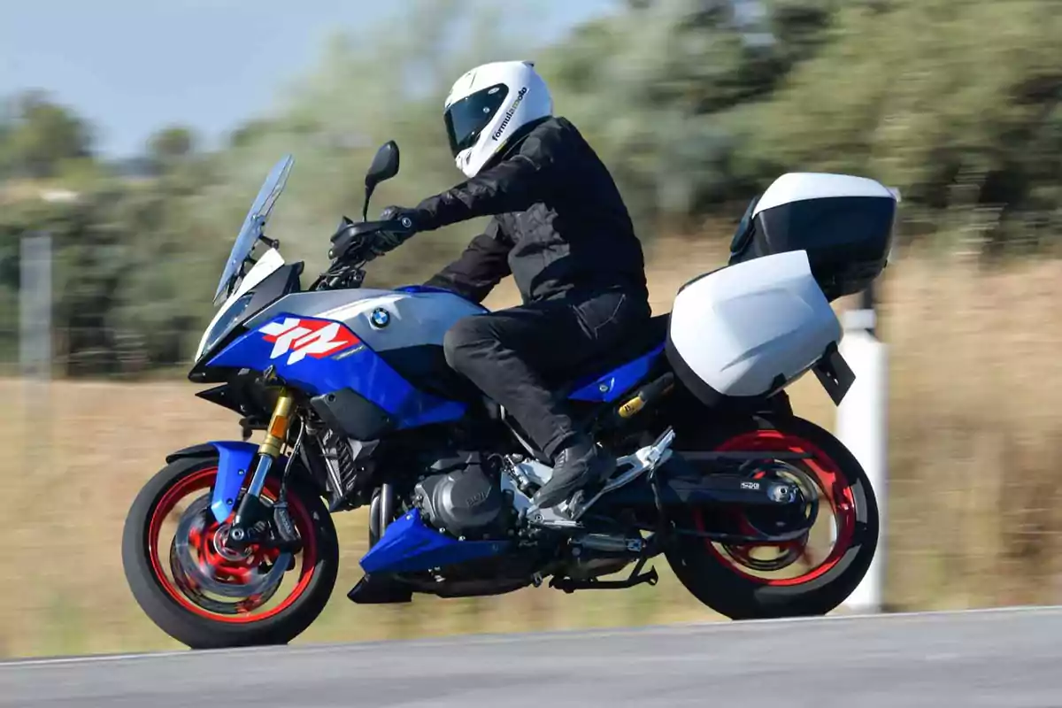 Persona conduciendo una motocicleta deportiva BMW azul con maletas laterales blancas en una carretera Persona conduciendo una motocicleta deportiva BMW azul con maletas laterales blancas en una carretera