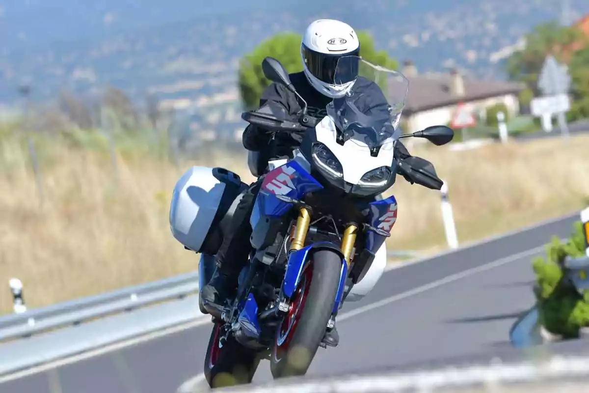 Persona conduciendo una motocicleta deportiva azul y blanca en una carretera curva con paisaje de fondo borroso Persona conduciendo una motocicleta deportiva azul y blanca en una carretera curva con paisaje de fondo borroso