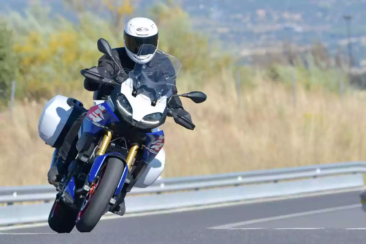 Persona conduciendo una motocicleta deportiva azul con maletas laterales en una carretera curva Persona conduciendo una motocicleta deportiva azul con maletas laterales en una carretera curva
