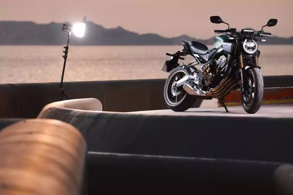 Motocicleta deportiva estacionada sobre una estructura de concreto junto al mar al atardecer con una luz de fotografía encendida a un lado Motocicleta deportiva estacionada sobre una estructura de concreto junto al mar al atardecer con una luz de fotografía encendida a un lado