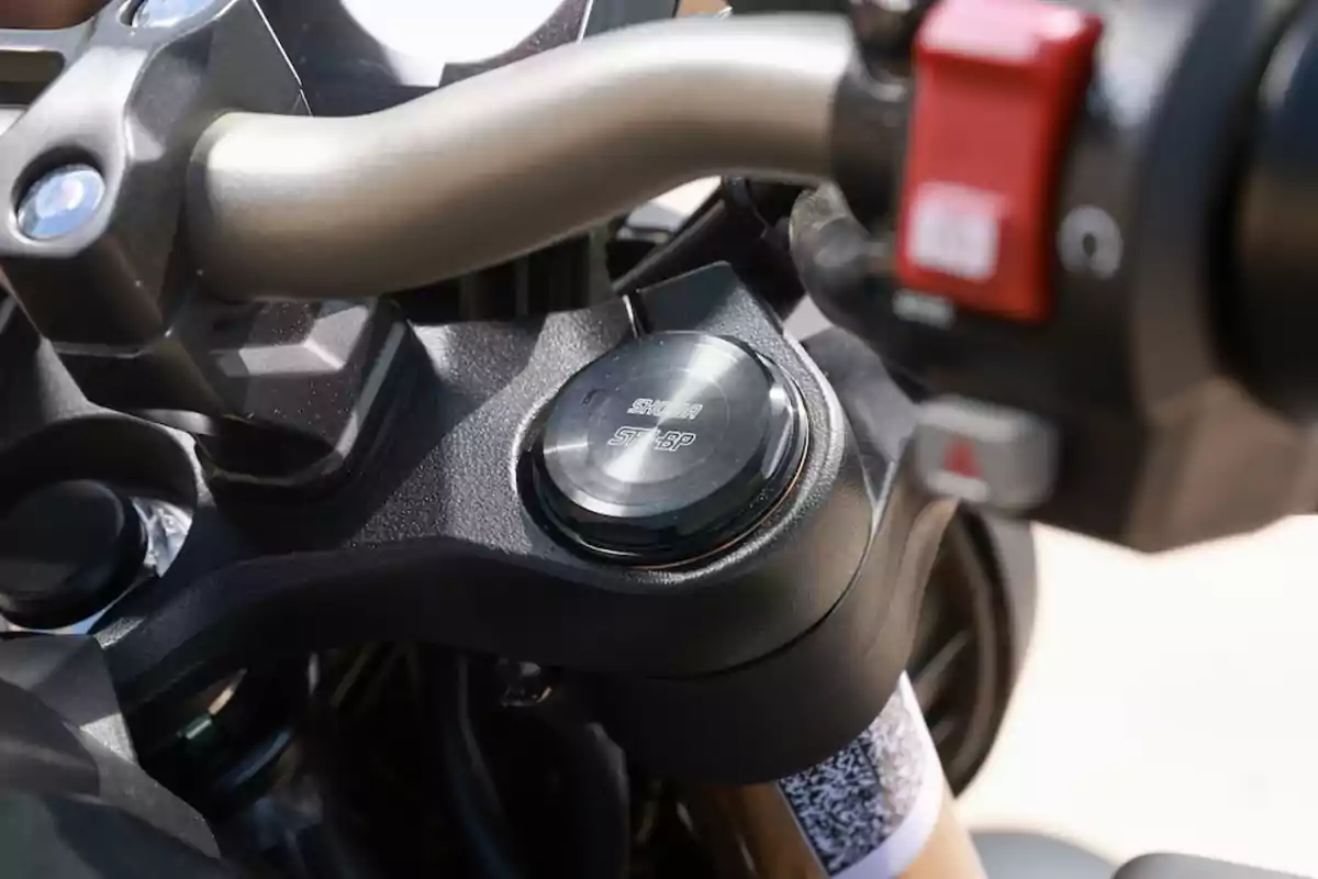Detalle del manillar de una motocicleta con enfoque en el tapón de la suspensión y el interruptor rojo en la empuñadura derecha Detalle del manillar de una motocicleta con enfoque en el tapón de la suspensión y el interruptor rojo en la empuñadura derecha