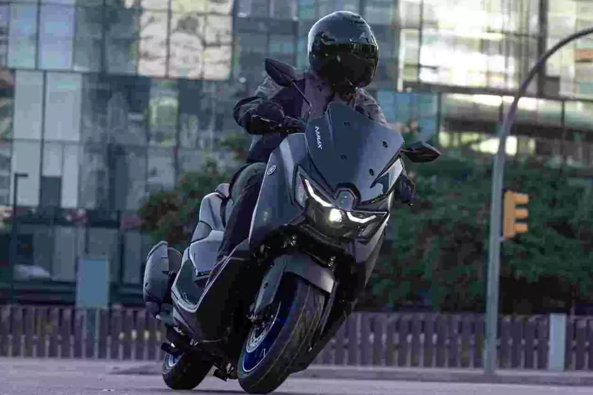 Persona conduciendo un Yanana MNAX 125 en una ciudad con edificios de fondo Persona conduciendo un Yanana MNAX 125 en una ciudad con edificios de fondo