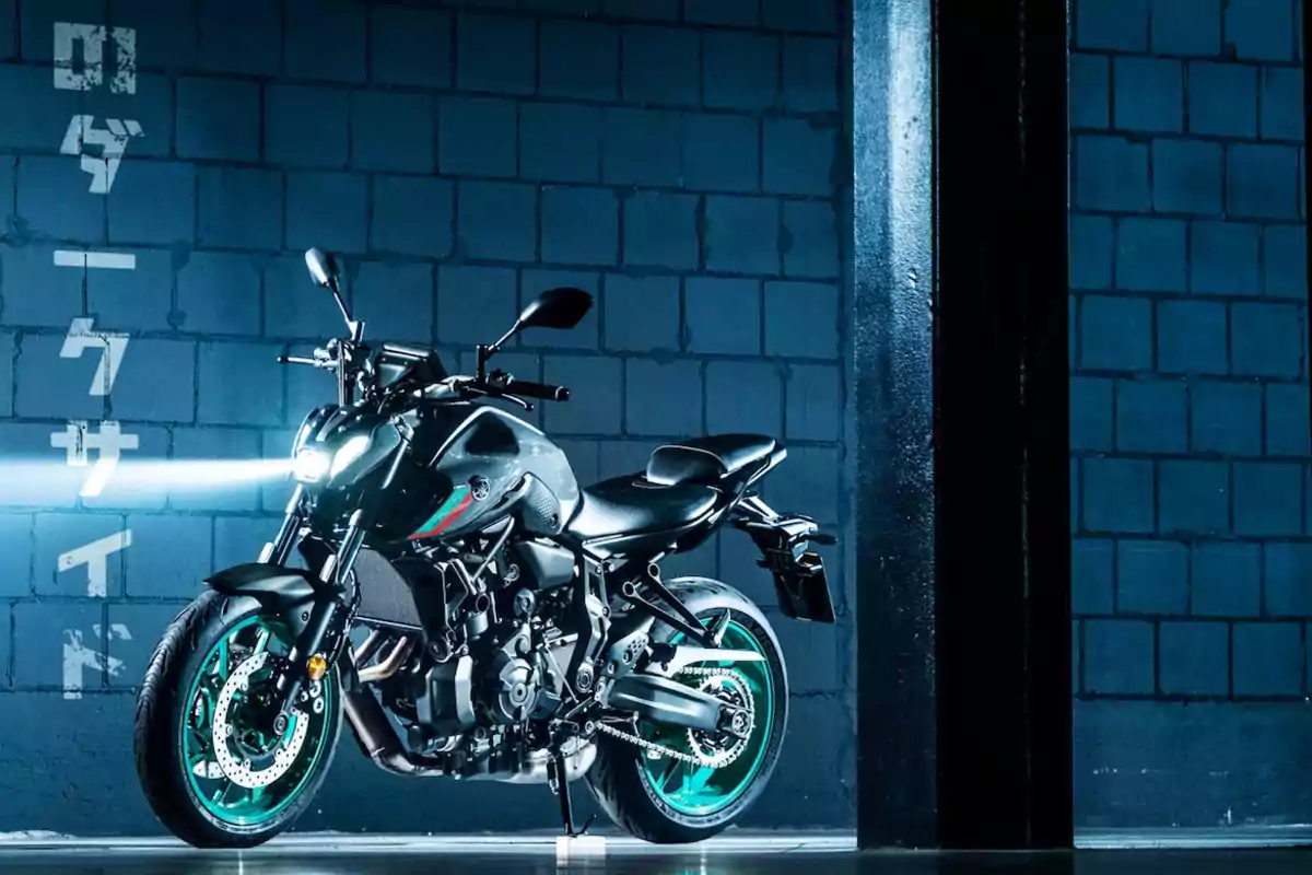 Motocicleta deportiva negra con rines verdes estacionada en un entorno industrial con paredes de bloques azules y luz encendida Motocicleta deportiva negra con rines verdes estacionada en un entorno industrial con paredes de bloques azules y luz encendida