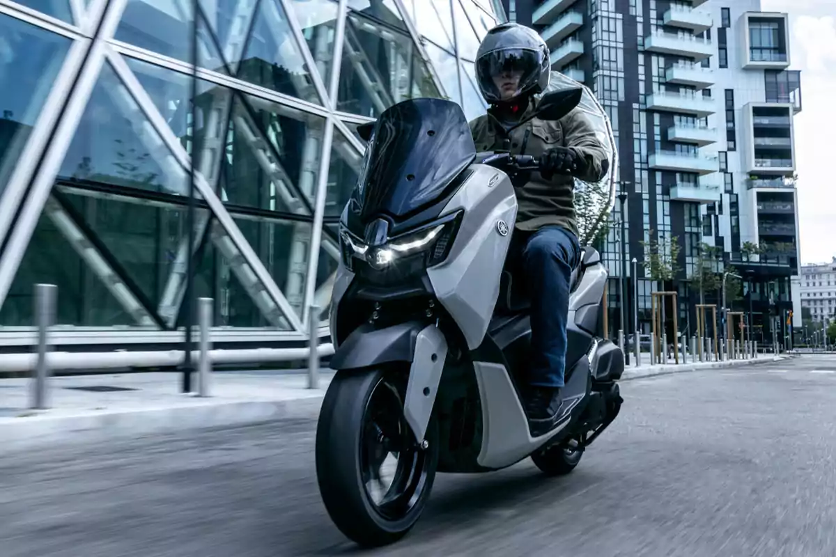 Persona conduciendo una motocicleta blanca por una ciudad moderna con edificios altos y fachadas de vidrio Persona conduciendo una motocicleta blanca por una ciudad moderna con edificios altos y fachadas de vidrio