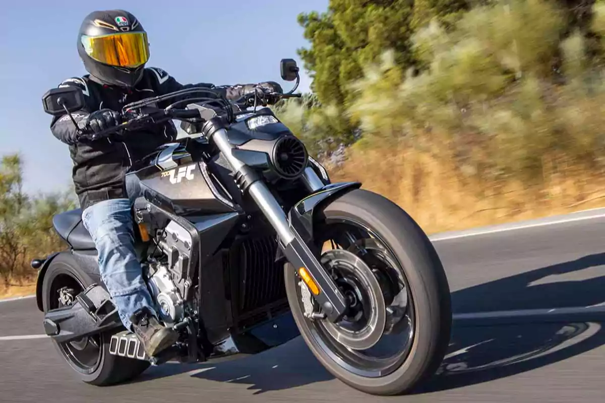 Persona conduciendo una motocicleta deportiva negra en una carretera con vegetación al fondo Persona conduciendo una motocicleta deportiva negra en una carretera con vegetación al fondo