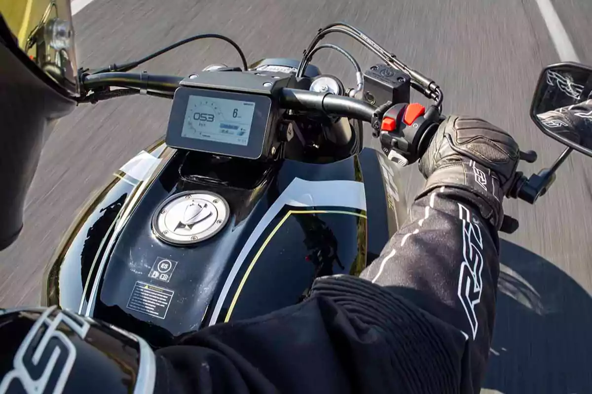 Persona conduciendo una motocicleta negra vista desde arriba con el velocímetro digital visible y guantes de protección Persona conduciendo una motocicleta negra vista desde arriba con el velocímetro digital visible y guantes de protección