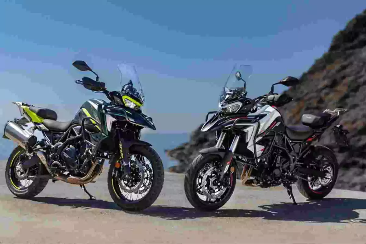 Dos motocicletas tipo adventure estacionadas sobre asfalto con un fondo de cielo azul y una colina rocosa. Dos motocicletas tipo adventure estacionadas sobre asfalto con un fondo de cielo azul y una colina rocosa.