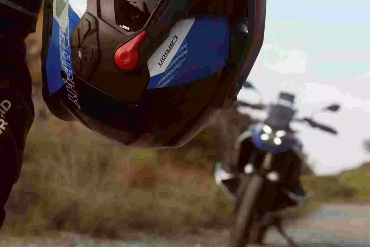 Person holding a motorcycle helmet with a blurred motorcycle in the background on an outdoor road Person holding a motorcycle helmet with a blurred motorcycle in the background on an outdoor road