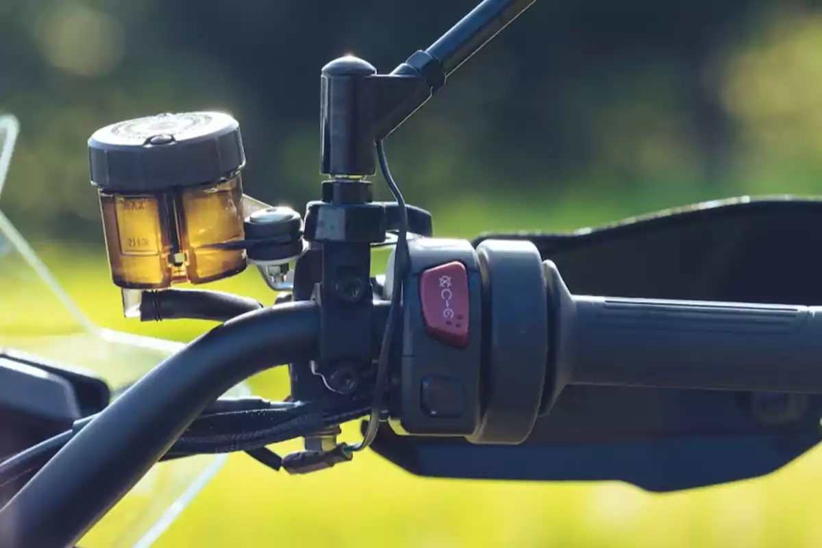 Manillar de motocicleta con depósito de líquido de frenos y botón de encendido rodeado de naturaleza desenfocada Manillar de motocicleta con depósito de líquido de frenos y botón de encendido rodeado de naturaleza desenfocada