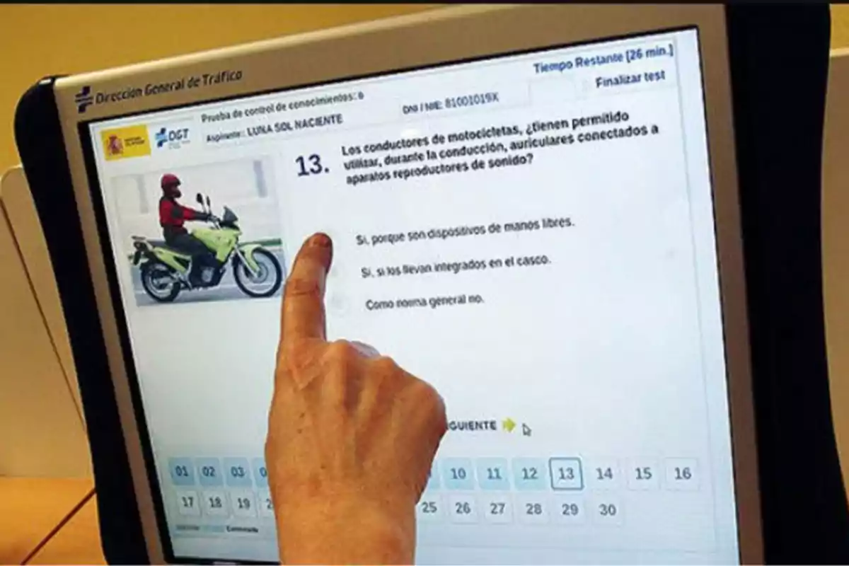 Person pointing at a computer screen while answering a theoretical motorcycle driving test question at the DGT