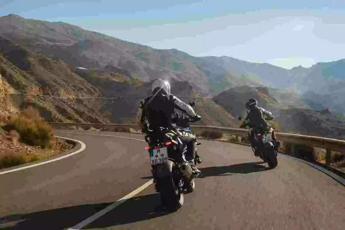 Dos personas conduciendo motocicletas en una carretera de montaña con curvas rodeadas de paisajes áridos y montañas al fondo Dos personas conduciendo motocicletas en una carretera de montaña con curvas rodeadas de paisajes áridos y montañas al fondo