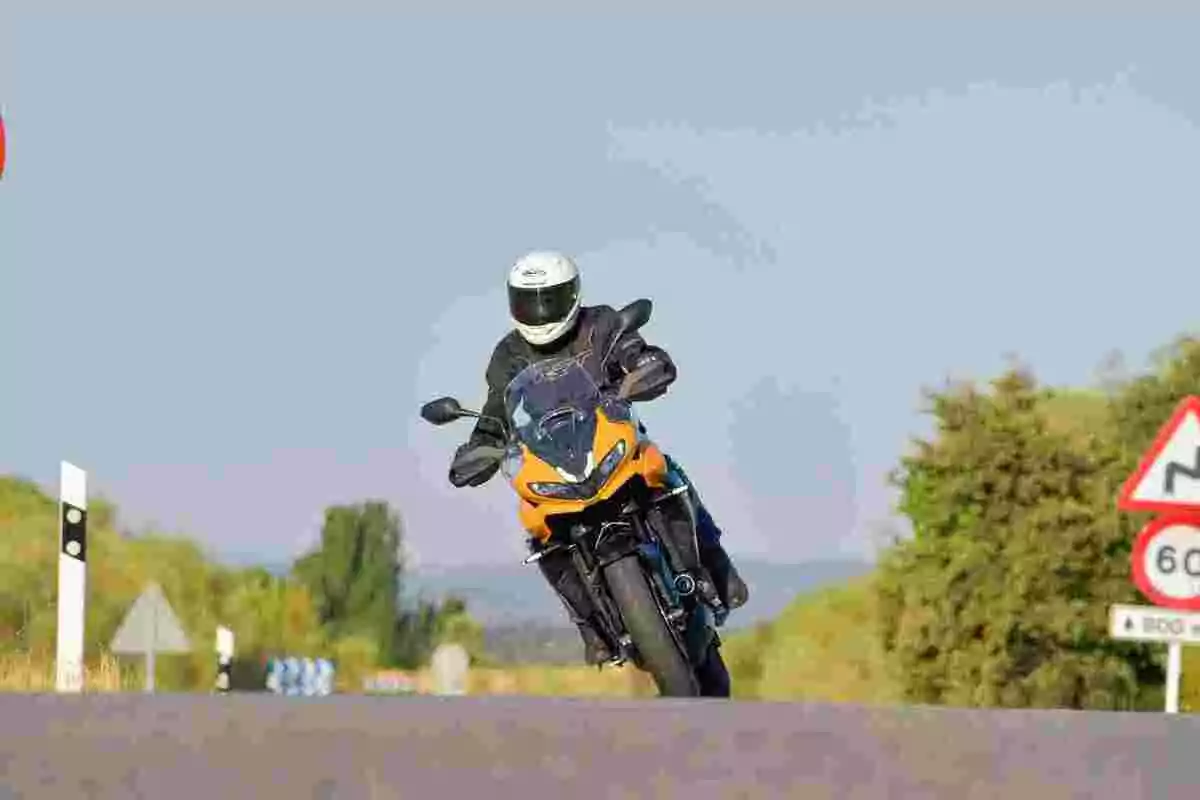 Persona conduciendo una motocicleta amarilla en una carretera con señales de tránsito y vegetación al fondo Persona conduciendo una motocicleta amarilla en una carretera con señales de tránsito y vegetación al fondo