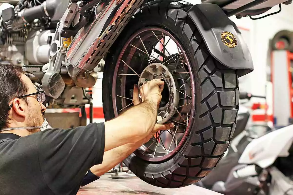 Hombre reparando la llanta trasera de una motocicleta en un taller mecánico Hombre reparando la llanta trasera de una motocicleta en un taller mecánico