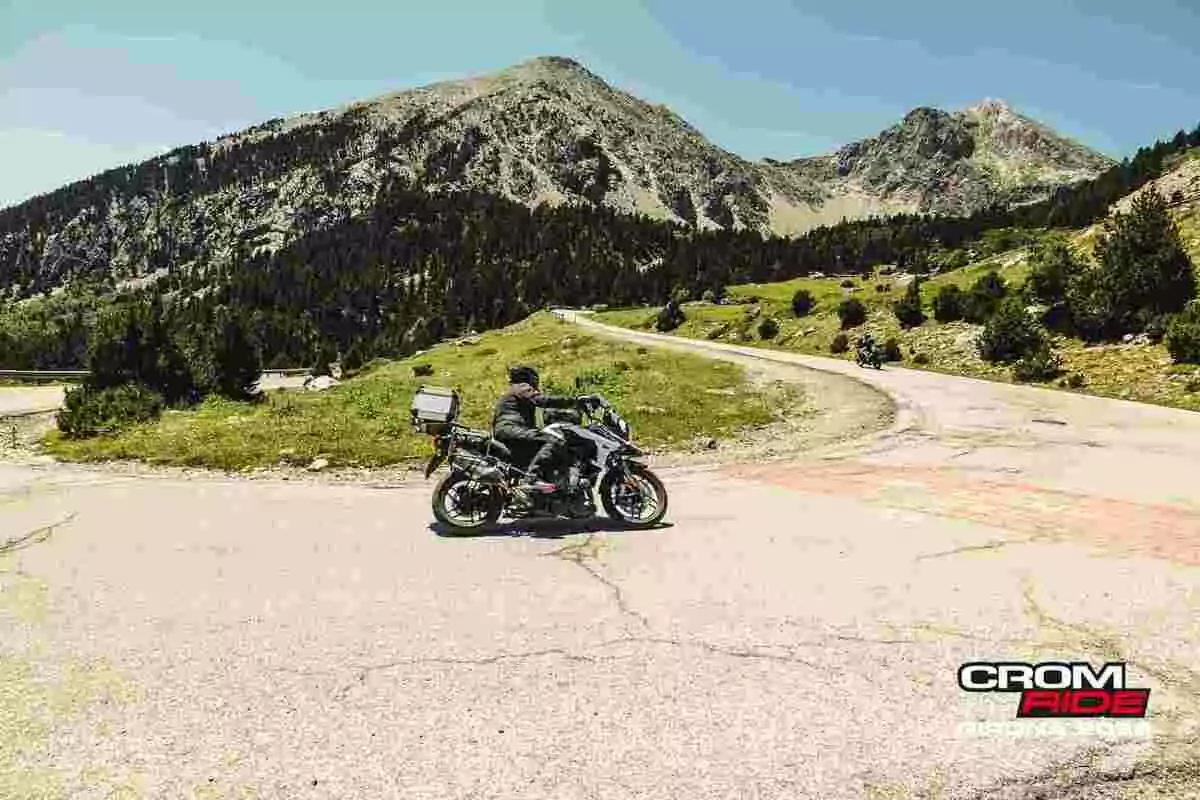 Motociclista recorriendo una carretera de montaña rodeada de vegetación y pinos bajo un cielo despejado Motociclista recorriendo una carretera de montaña rodeada de vegetación y pinos bajo un cielo despejado