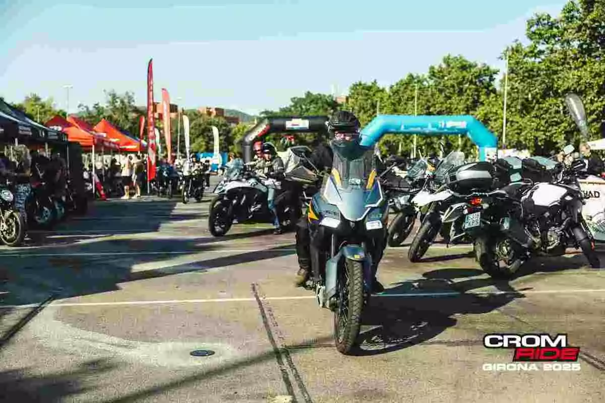 Evento de motociclismo al aire libre con varias motos y personas reunidas en un ambiente soleado rodeado de carpas y banderas promocionales Evento de motociclismo al aire libre con varias motos y personas reunidas en un ambiente soleado rodeado de carpas y banderas promocionales