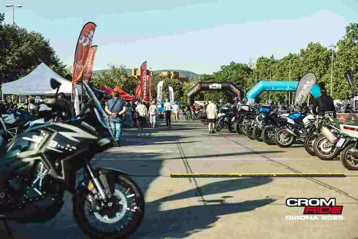 Evento de motociclismo al aire libre con varias motos estacionadas, personas caminando y carpas de diferentes marcas en un ambiente soleado Evento de motociclismo al aire libre con varias motos estacionadas, personas caminando y carpas de diferentes marcas en un ambiente soleado