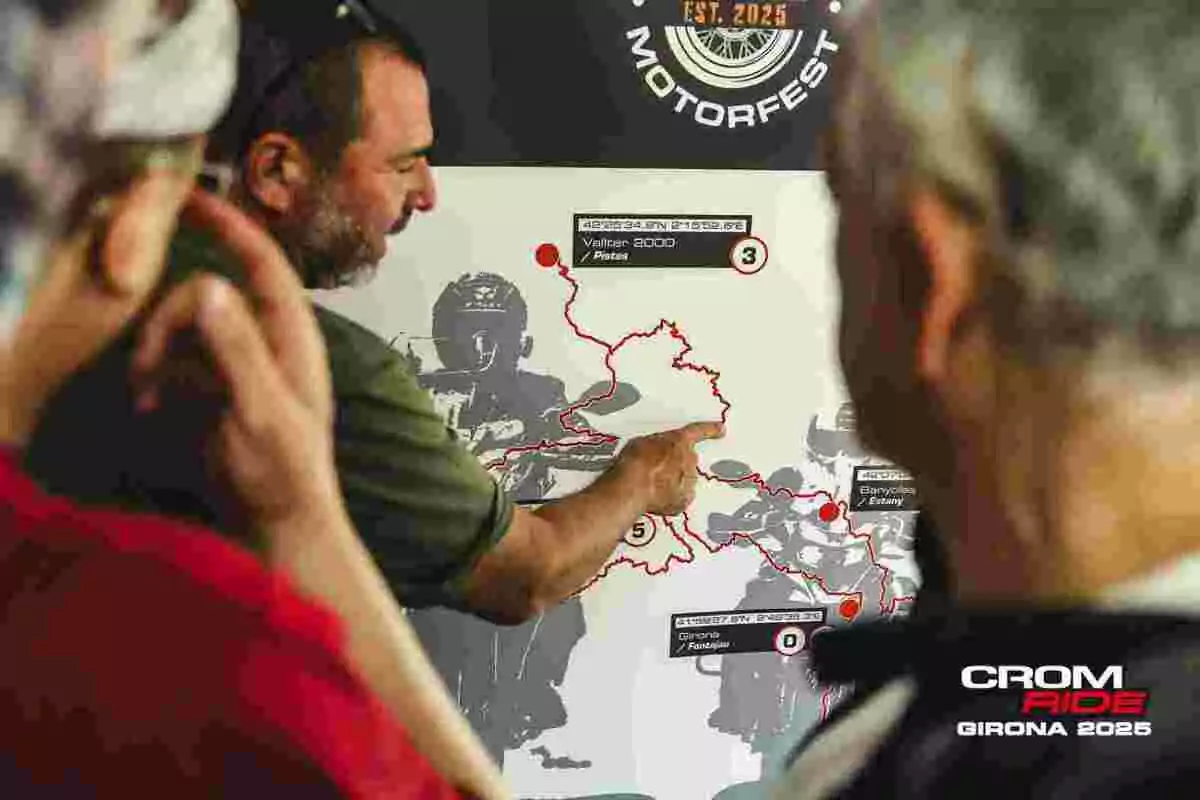 Un hombre señala una ruta en un mapa durante un evento de motociclismo mientras otras personas observan atentamente Un hombre señala una ruta en un mapa durante un evento de motociclismo mientras otras personas observan atentamente