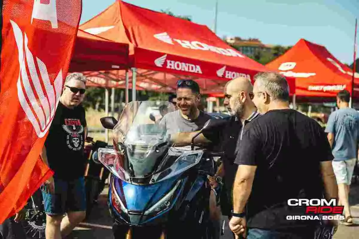 Cuatro hombres observan una motocicleta azul en un evento al aire libre con carpas rojas de Honda y ambiente soleado Cuatro hombres observan una motocicleta azul en un evento al aire libre con carpas rojas de Honda y ambiente soleado