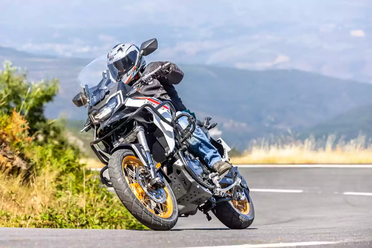 Persona conduciendo una motocicleta deportiva en una carretera de montaña con paisaje de fondo y vegetación a los lados