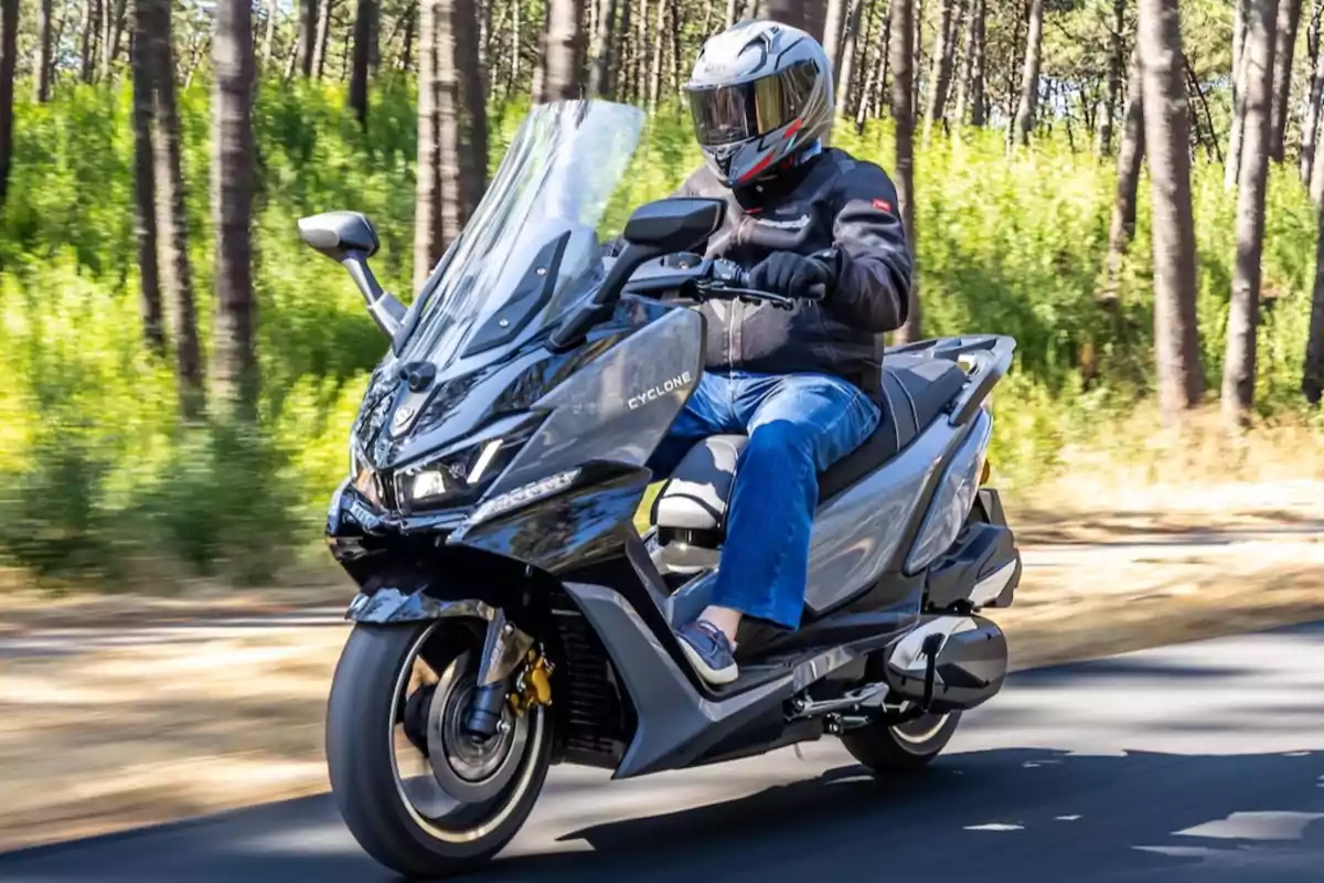 Persona conduciendo una motocicleta tipo scooter en una carretera rodeada de árboles y vegetación