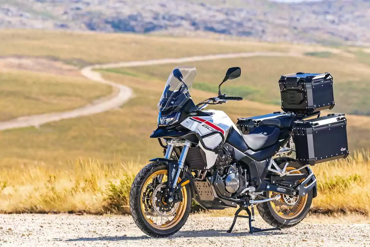 Motocicleta de aventura estacionada en un camino de tierra con maletas laterales y paisaje de campo al fondo Motocicleta de aventura estacionada en un camino de tierra con maletas laterales y paisaje de campo al fondo