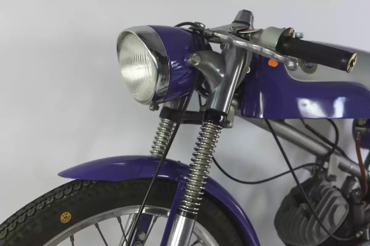 Motocicleta clásica de color morado vista desde el frente enfocando el faro, el manillar y parte del motor Motocicleta clásica de color morado vista desde el frente enfocando el faro, el manillar y parte del motor