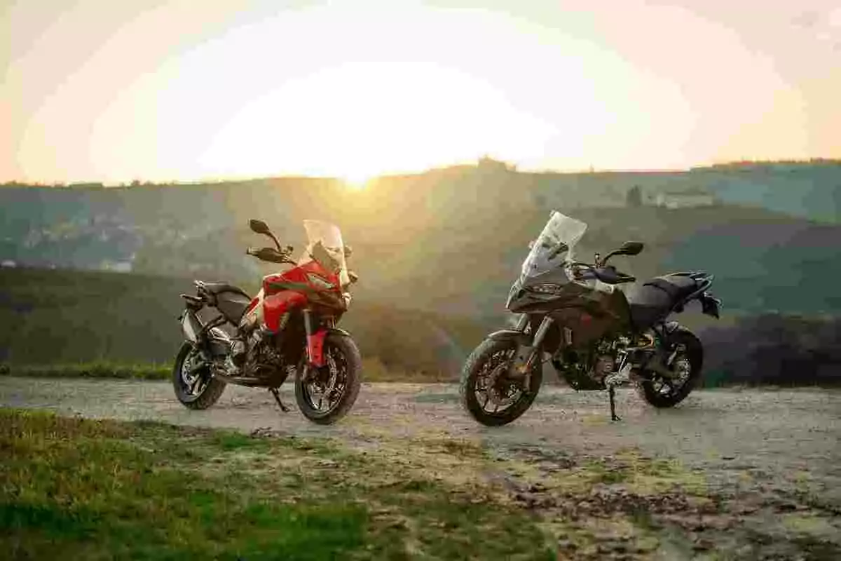 Dos motocicletas estacionadas en un camino de tierra con un paisaje de colinas al fondo y el sol poniéndose en el horizonte Dos motocicletas estacionadas en un camino de tierra con un paisaje de colinas al fondo y el sol poniéndose en el horizonte