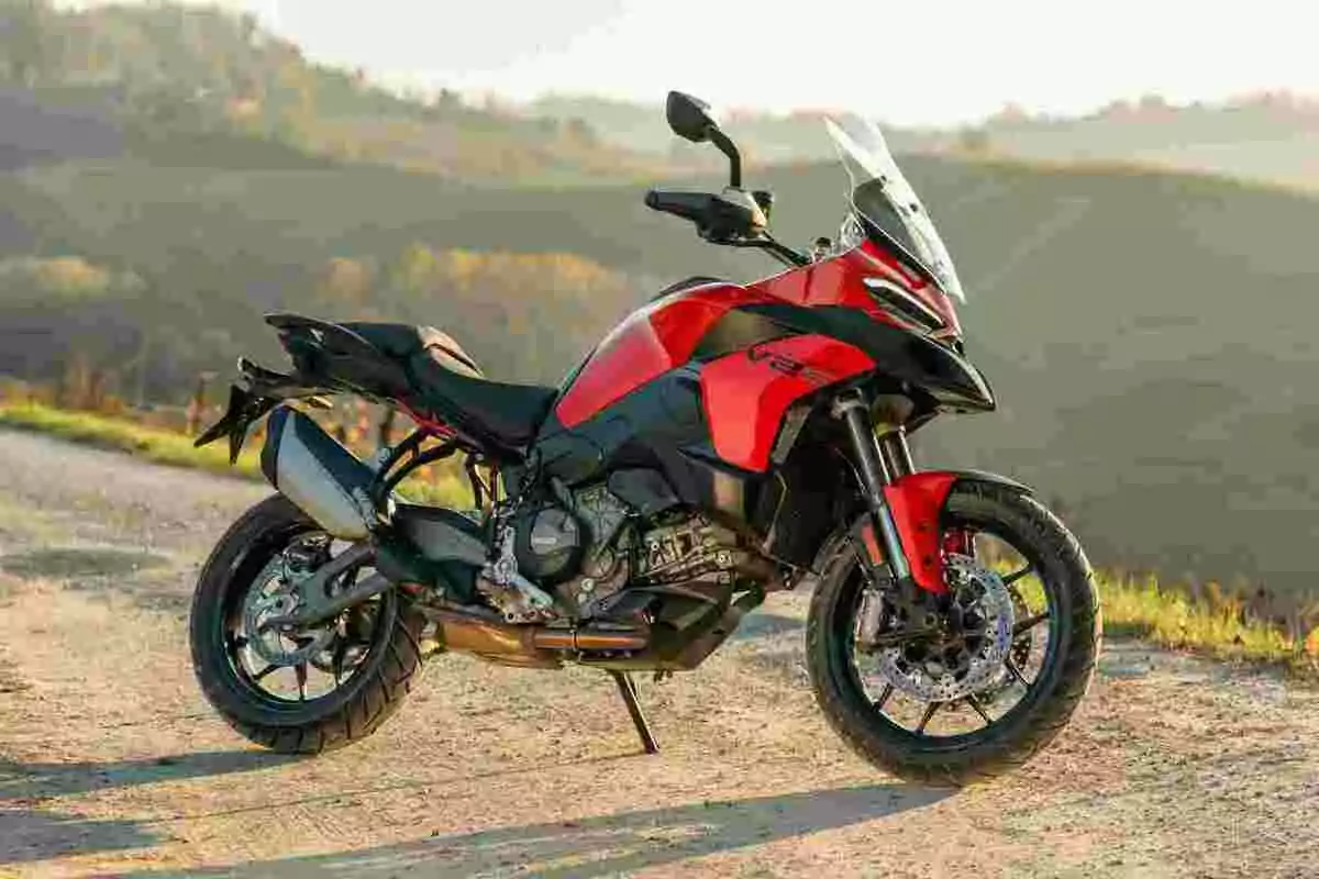 Motocicleta deportiva roja y negra estacionada en un camino de tierra con paisaje de colinas al fondo Motocicleta deportiva roja y negra estacionada en un camino de tierra con paisaje de colinas al fondo