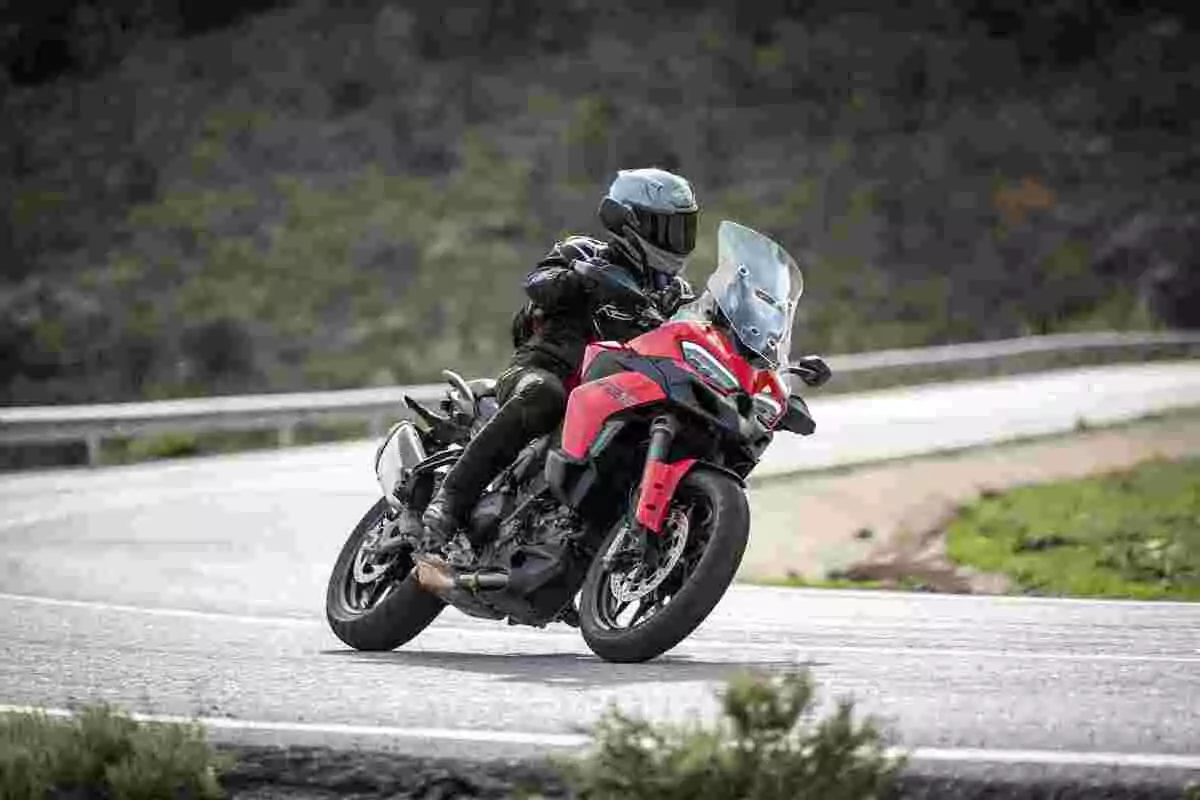 Persona conduciendo una motocicleta roja en una carretera curva rodeada de vegetación