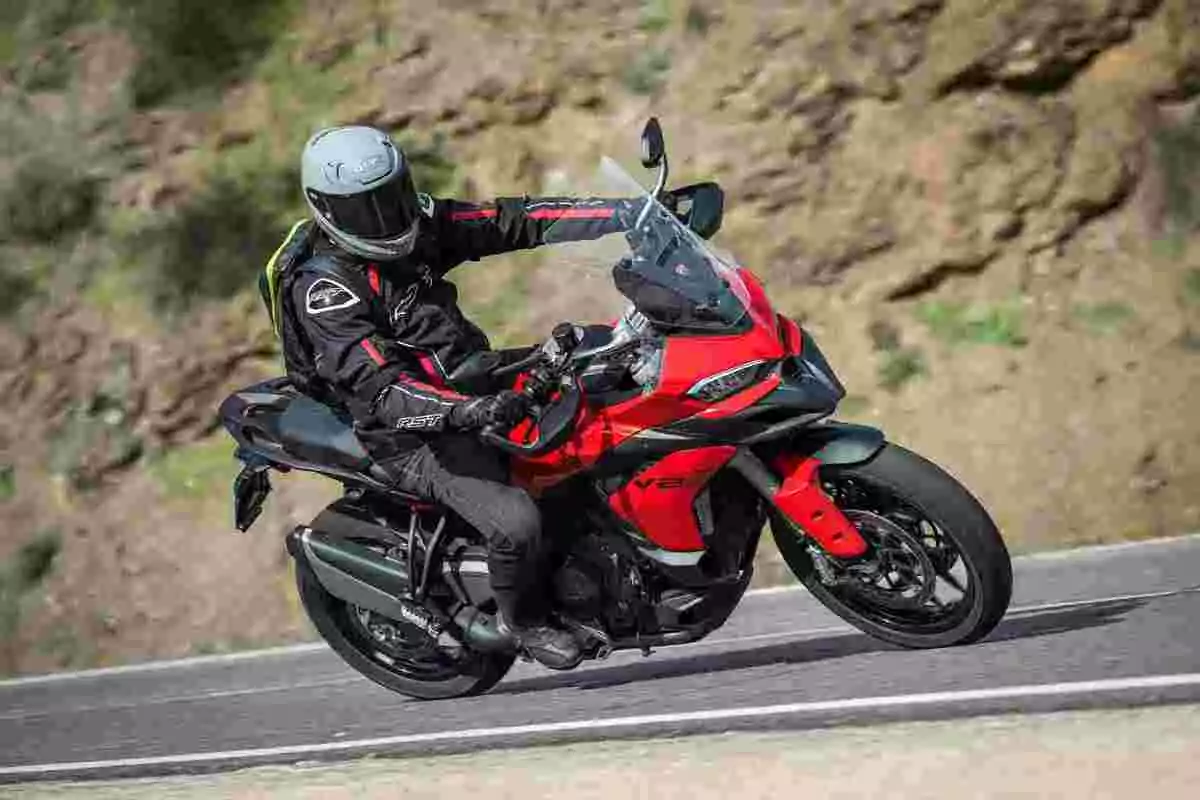 Persona con casco y equipo de protección conduciendo una motocicleta deportiva roja en una carretera curva Persona con casco y equipo de protección conduciendo una motocicleta deportiva roja en una carretera curva