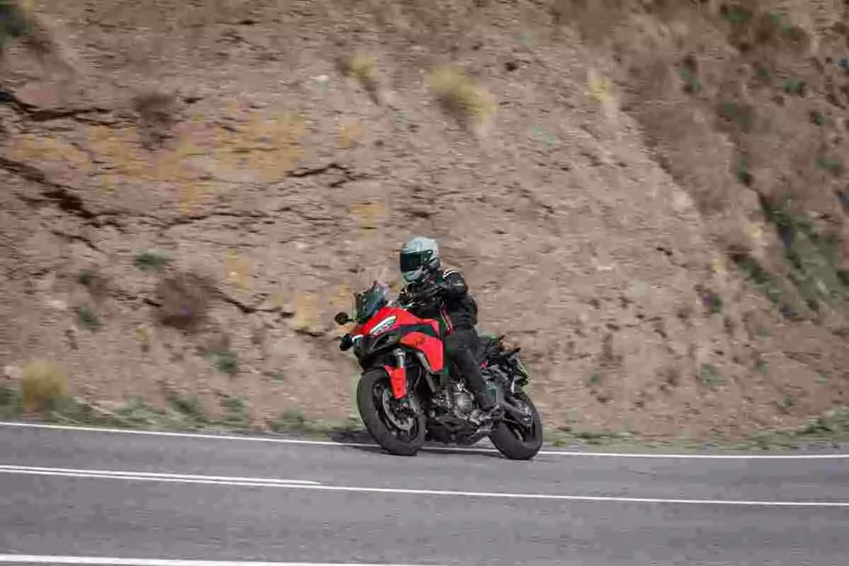 Persona con casco y ropa de protección conduciendo una motocicleta roja en una carretera de montaña Persona con casco y ropa de protección conduciendo una motocicleta roja en una carretera de montaña