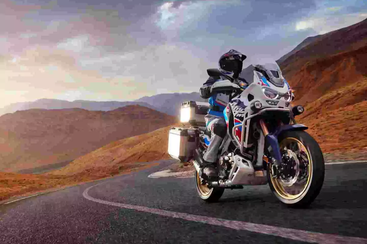 Motociclista conduciendo una moto de aventura en una carretera de montaña al atardecer Motociclista conduciendo una moto de aventura en una carretera de montaña al atardecer