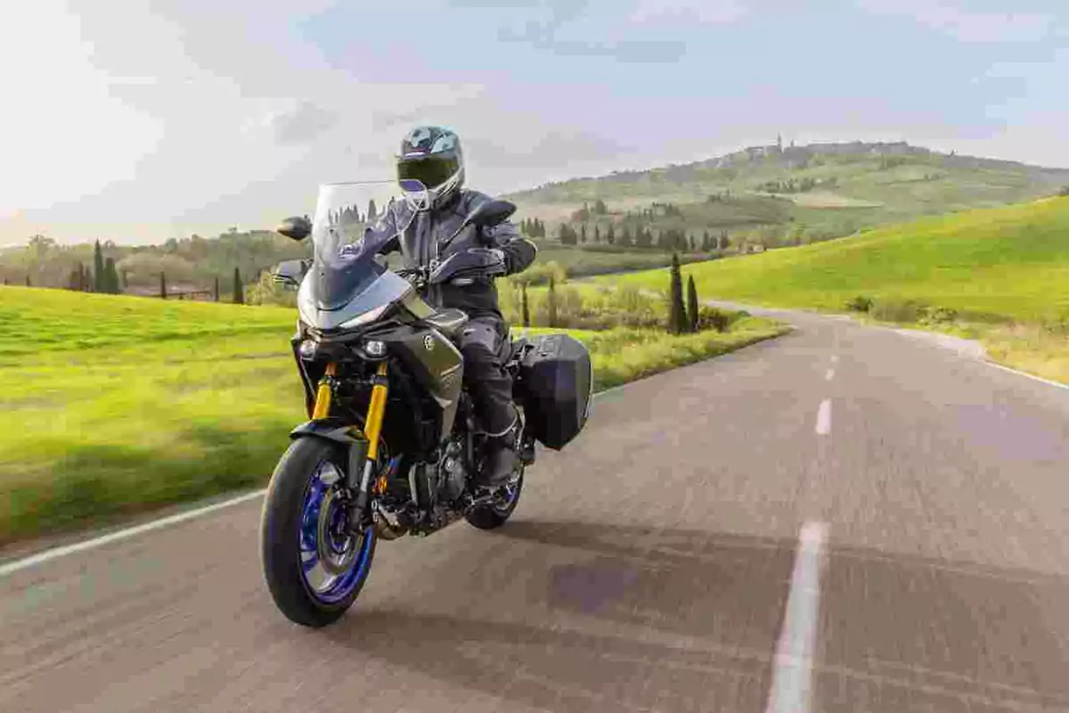 Persona conduciendo una motocicleta en una carretera rodeada de colinas verdes bajo un cielo despejado Persona conduciendo una motocicleta en una carretera rodeada de colinas verdes bajo un cielo despejado