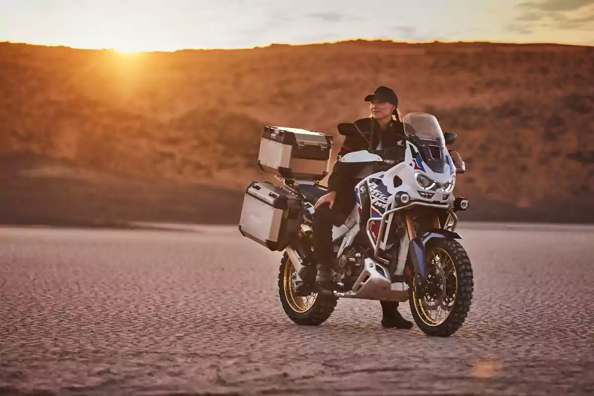 Mujer con ropa de motociclista sentada en una moto de aventura en un paisaje desértico al atardecer Mujer con ropa de motociclista sentada en una moto de aventura en un paisaje desértico al atardecer